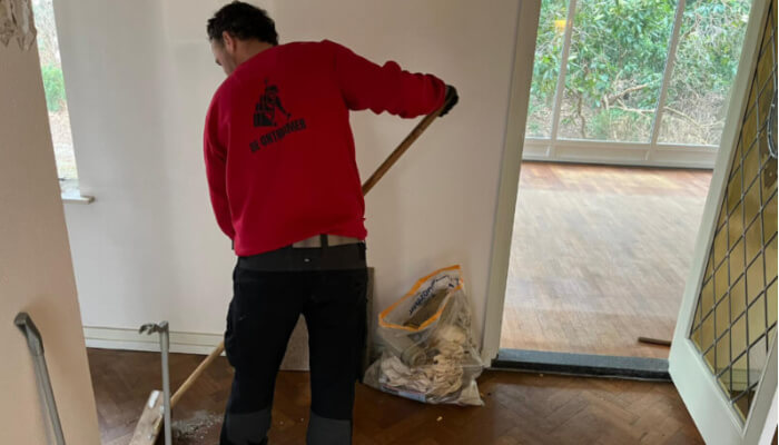 De ontruimer bezemt de vloer van een woning